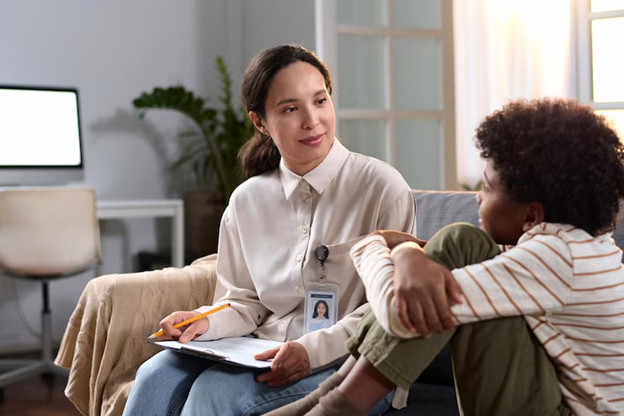female profession sits on couch and talks with child with pen and notepad in hand