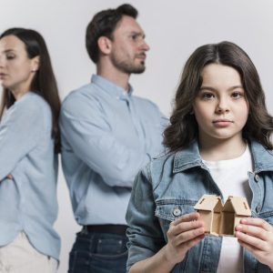 girl holding a broken home with parents in the background
