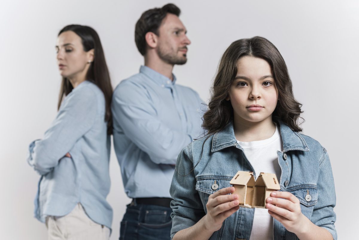 girl holding a broken home with parents in the background