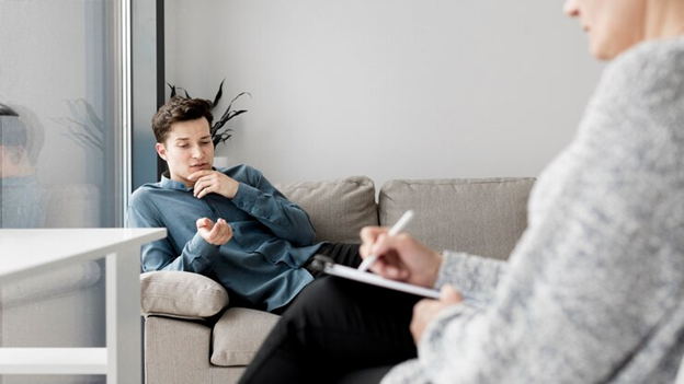 man laying on couch talking with someone in a chair with pen and notepad