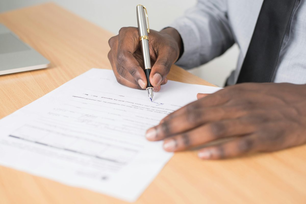 person holding a gray twist pen and white paper writing on brown wooden table
