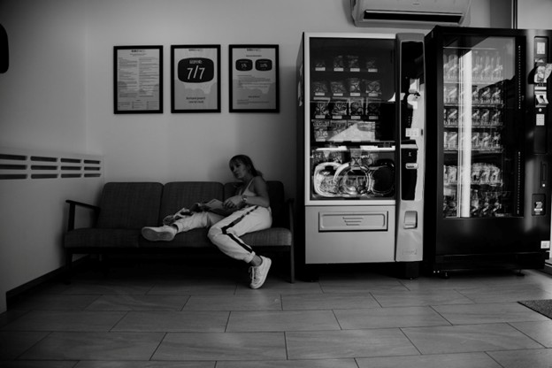 black and white photo of girl sitting on couch next to vending machines