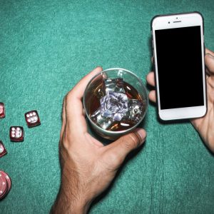 man holding phone and drink at a poker table at a casino