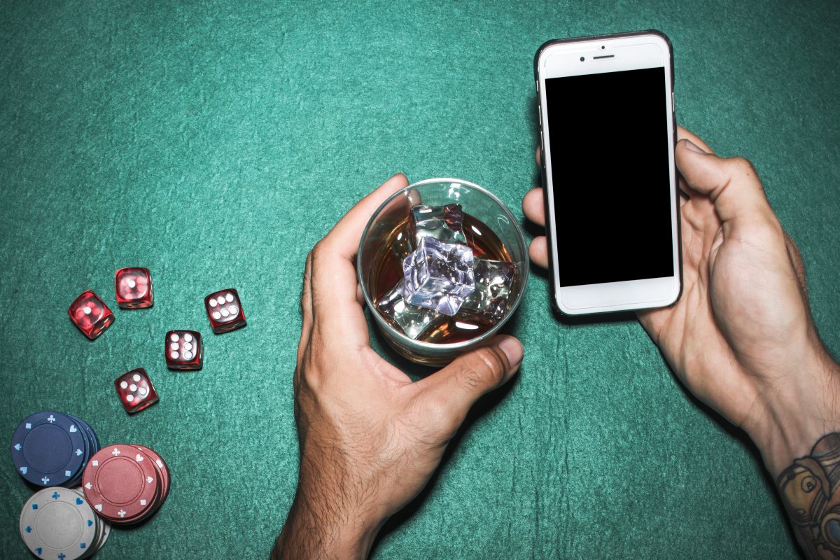 man holding phone and drink at a poker table at a casino
