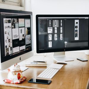two apple computer screens sitting on a wooden desk