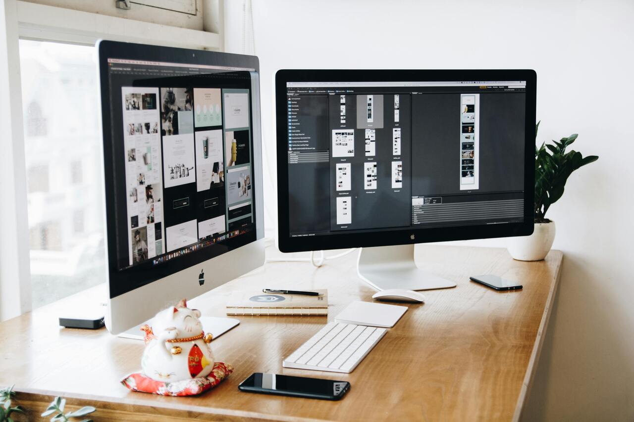 two apple computer screens sitting on a wooden desk