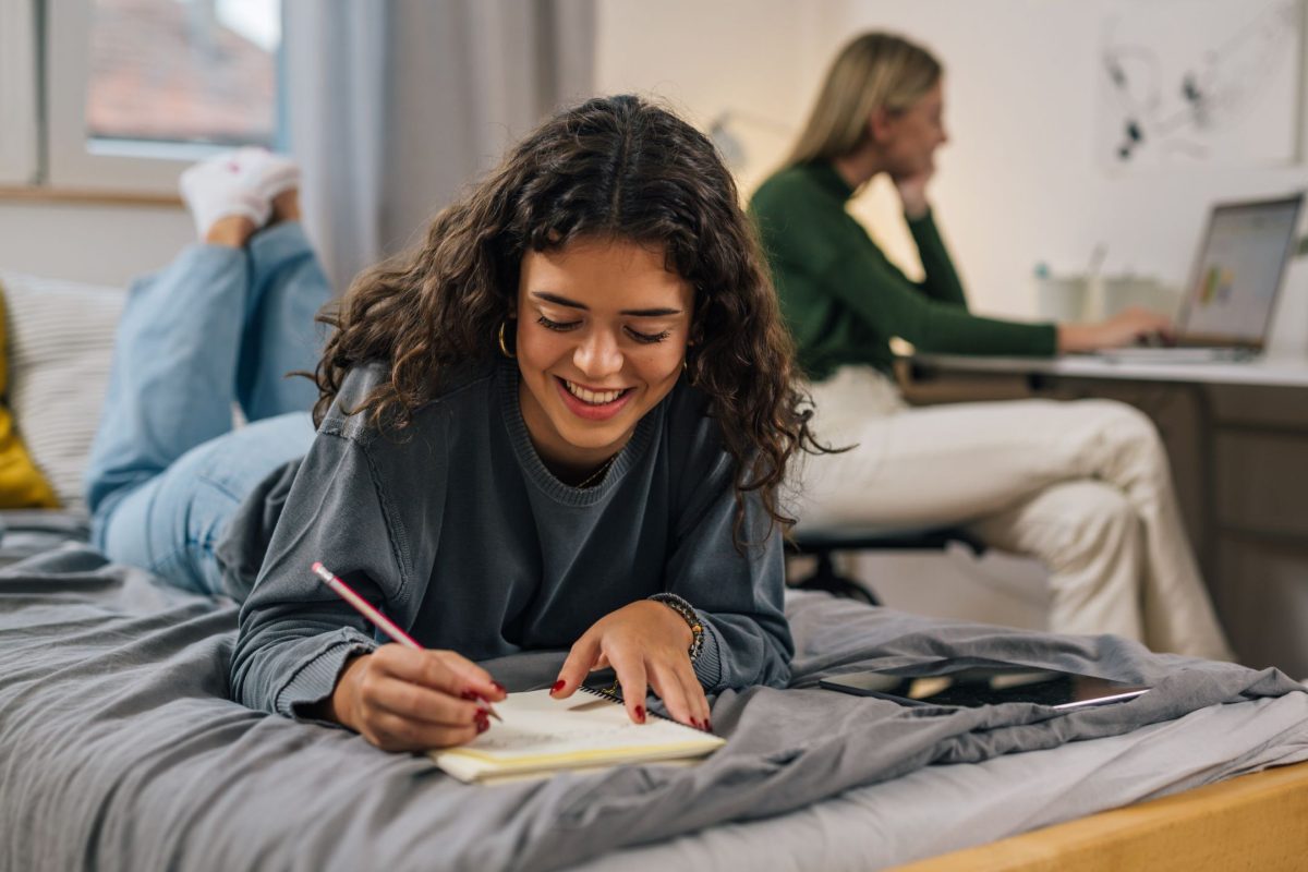 girl laying in the bed writing in a notebook