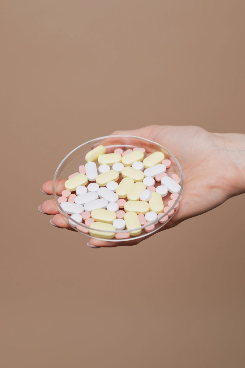 hand holding a glass container with a variety of medication pills and tablets