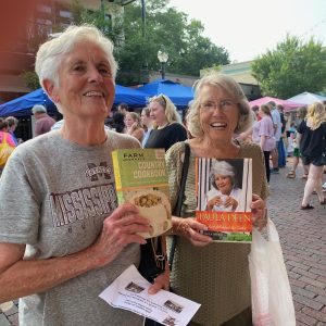 Roz Watkins (left) and Gracie McClendon (right) display their books of choice from the Friends of the Library table at the first Fresh at Five event. The library support organization brought cookbooks, in keeping with the fresh garden offerings and other delicacies available at the market.