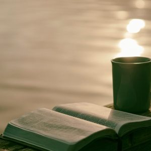 open bible and a cup of coffee on railing near the water
