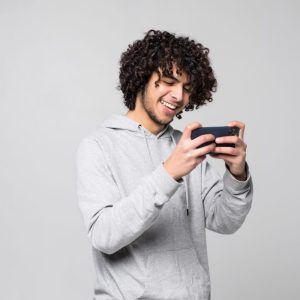 young man with curly hair using smartphone with gray wall background