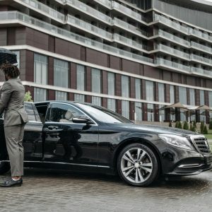 man holding open a car door and holding an umbrella for a lady