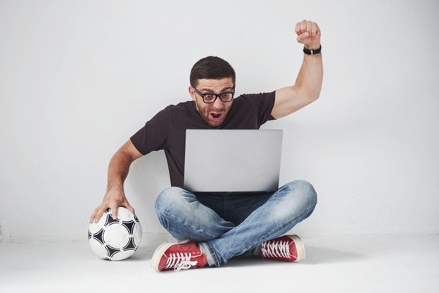 man sitting on the floor crosslegged with soccer ball and computer and fist raised in the air