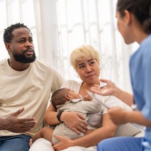 mom, dad and baby sit on a couch and talk with a nurse.
