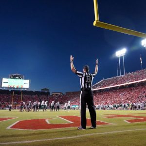 referee standing at a football goal post with hands in the air