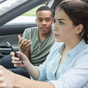 woman and man sitting in a car. WOman holding a phone and driving