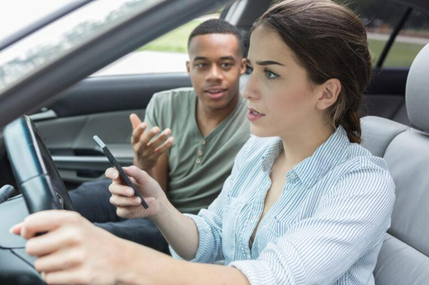 woman and man sitting in a car. WOman holding a phone and driving