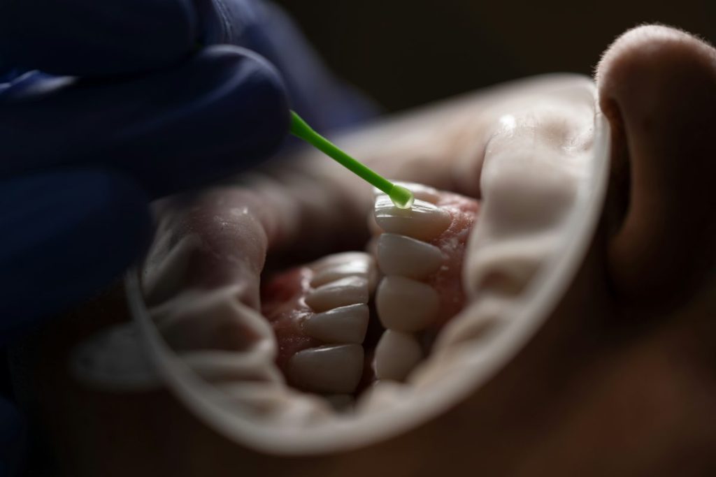 a person holding a green tube on someones teeth