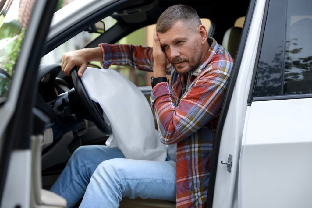 A man near an opened airbag holding his head after a car accident