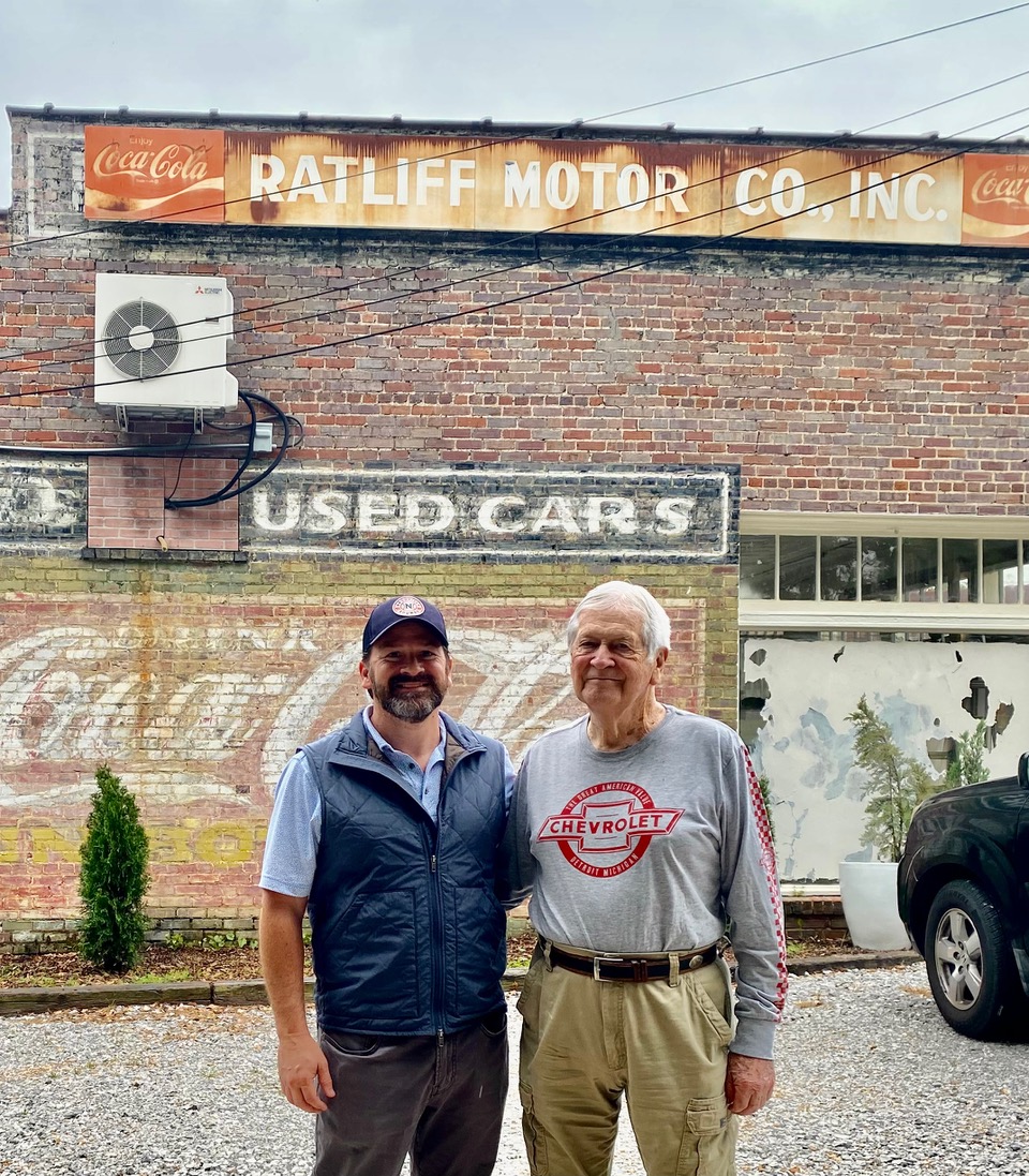 Ed Ratliff (right) and his son Greg (left) are shown with signs of past times on the 1927 building that has housed many businesses over the years, beginning with Ratliff Motor Company.