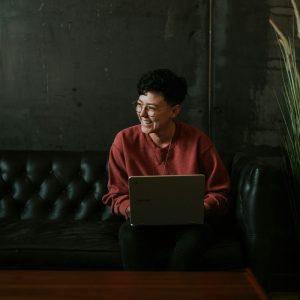 Smiling man using laptop computer while sitting on black leather sofa photo