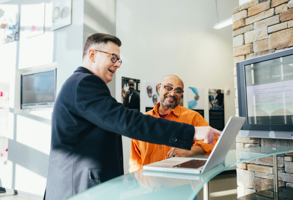 male professional pointing at laptop screen while talking with a customer sitting at a counter