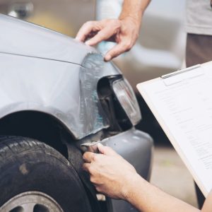 insurance agent looking at a car after a car accident with paperwork in hand