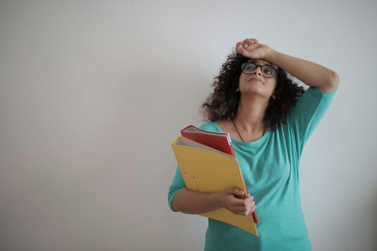 woman in green top holding binders with hand on head feeling anxious