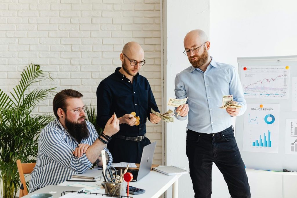 three male professionals in an office counting money