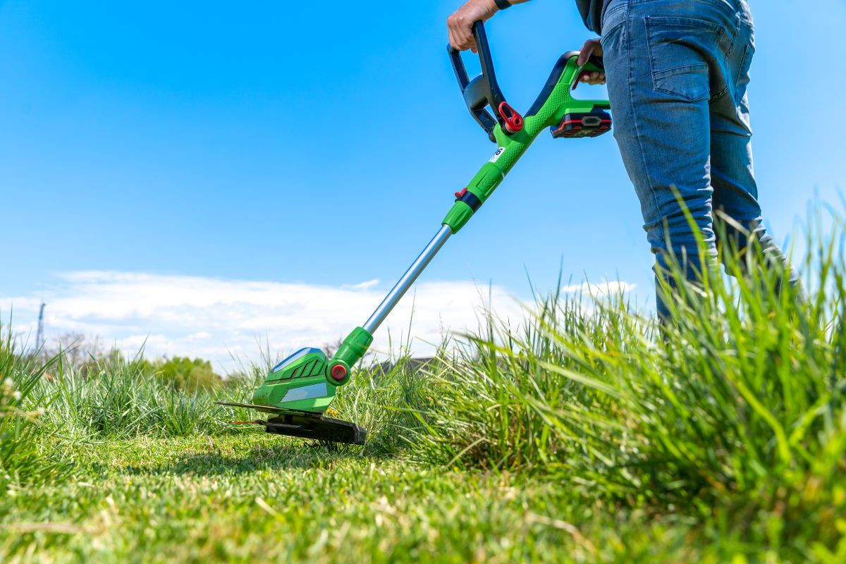 man mows grass meadow with hand held cordless weedeater mower