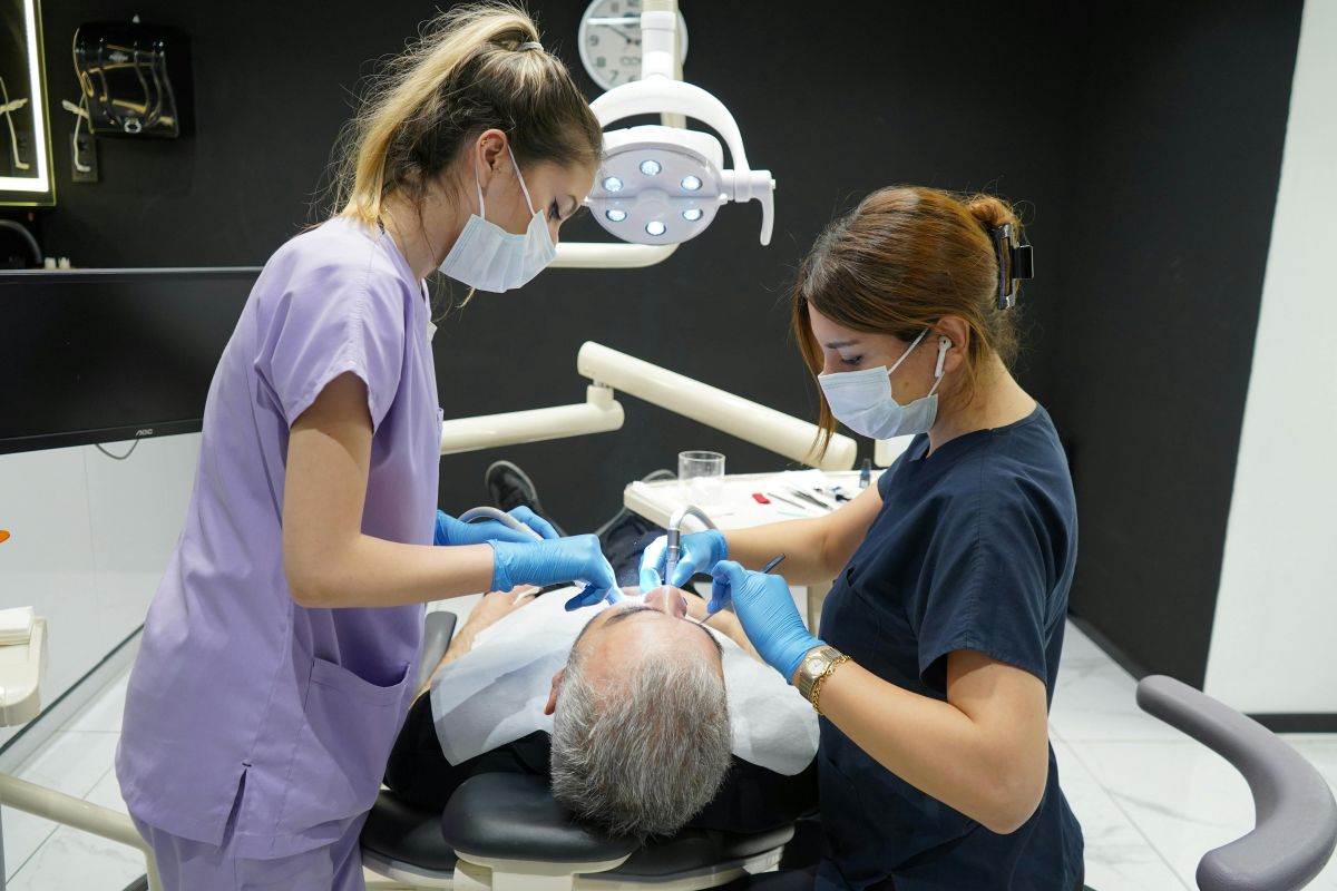 dentist and dental hygienist clean male patient's mouth