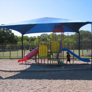 A playground with sliding equipment under a shade.