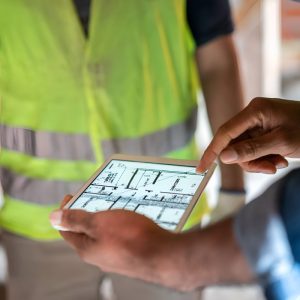close up of man holding a tablet with construction worker in yellow vest overlooks