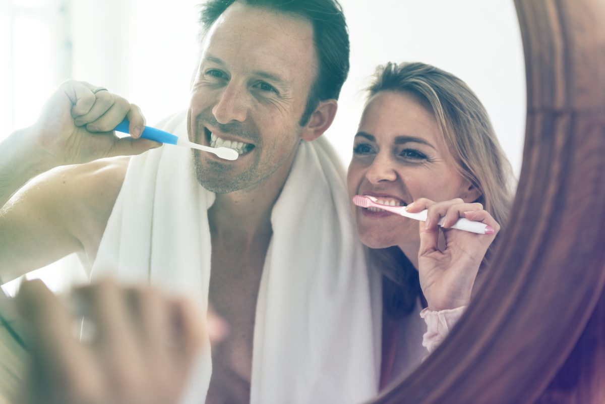 couple brush teeth in front of bathroom mirror