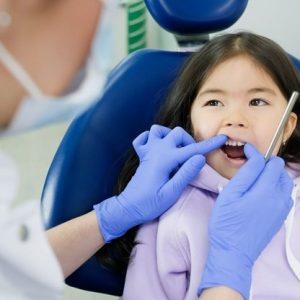 little girl sitting in dental chair with dentist looking at teeth