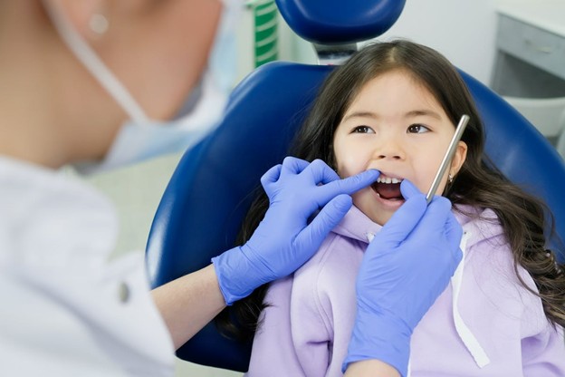 little girl sitting in dental chair with dentist looking at teeth