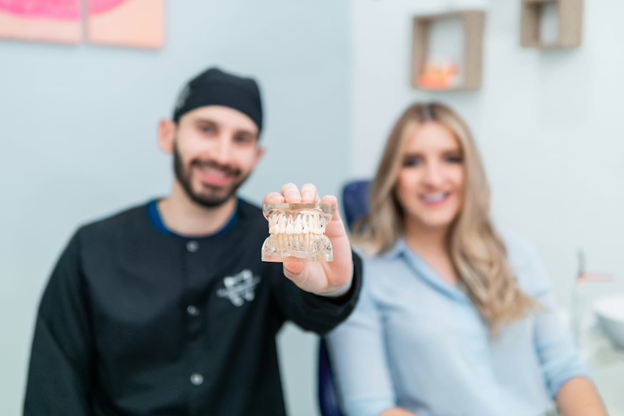 male dentist hold dental molding to camera sitting with female patient
