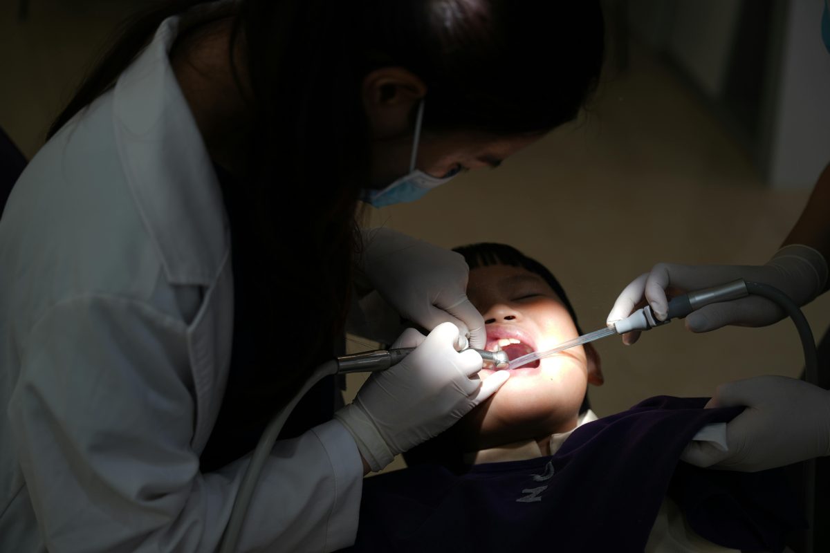 kid at dentist with dentist looking in his mouth using suction and water