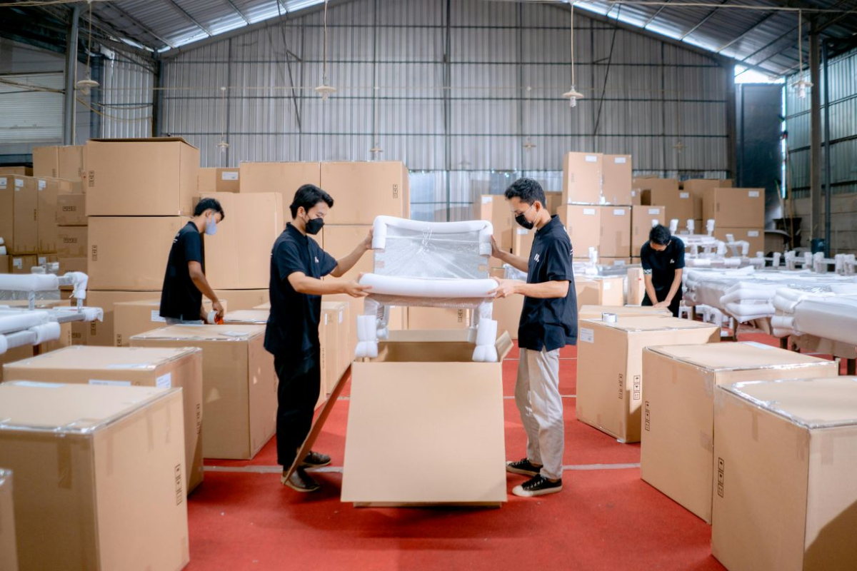 men in black uniforms place chair in box in a warehouse full of boxes