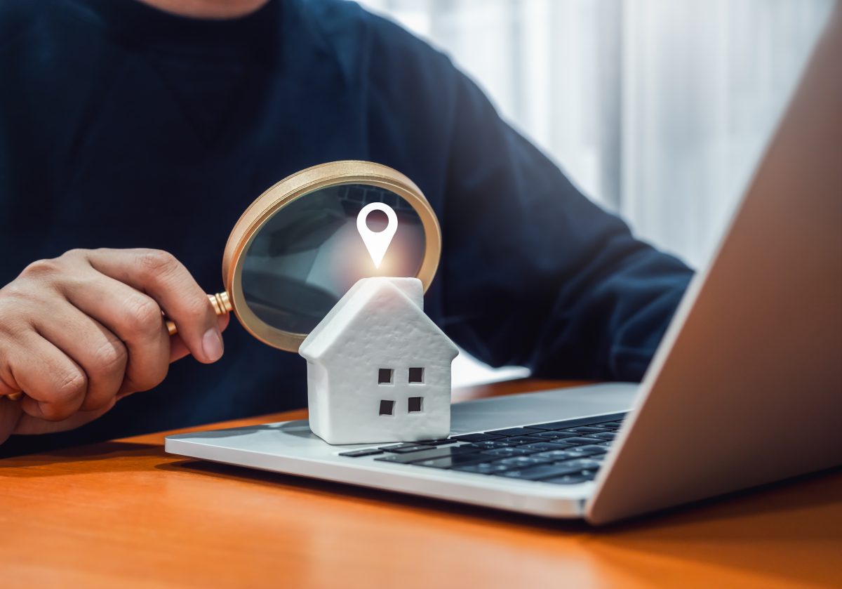 man holding a magnifying glass at a small house sitting on an open laptop