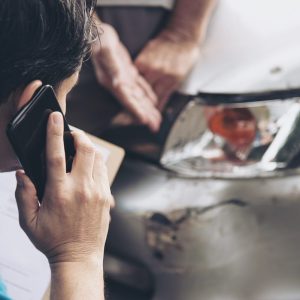 man on the phone with insurance while looking at damage to vehicle