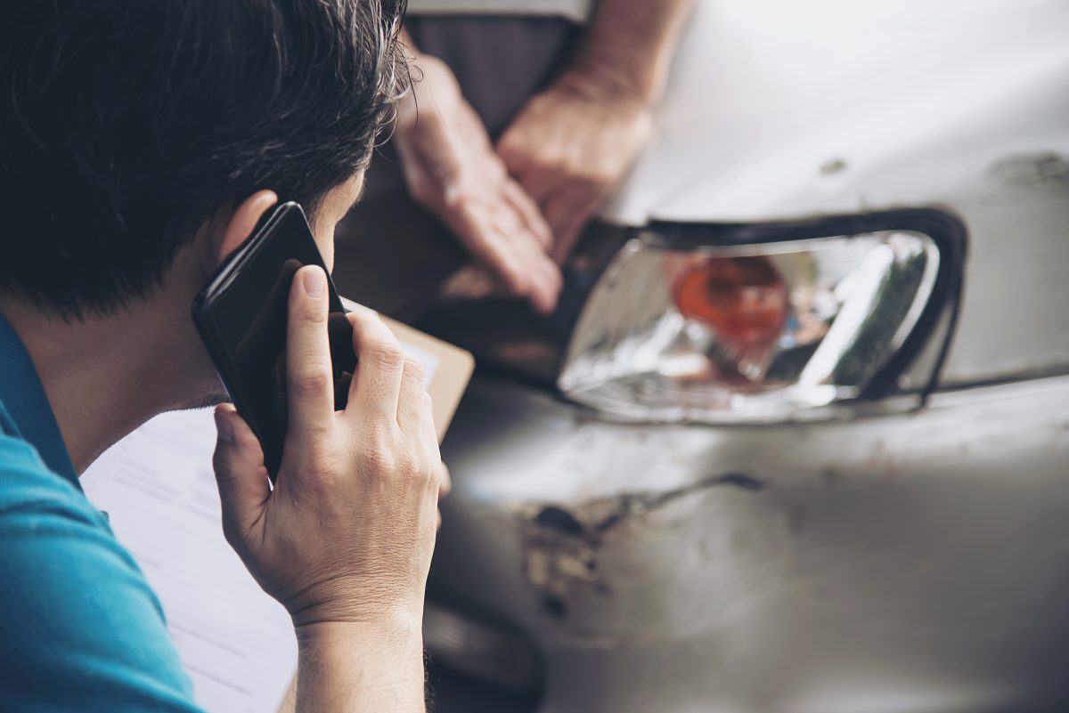 man on the phone with insurance while looking at damage to vehicle