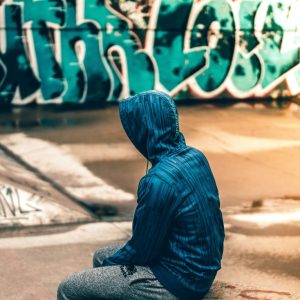 a person in a blue jacket sitting near a graffitied wall