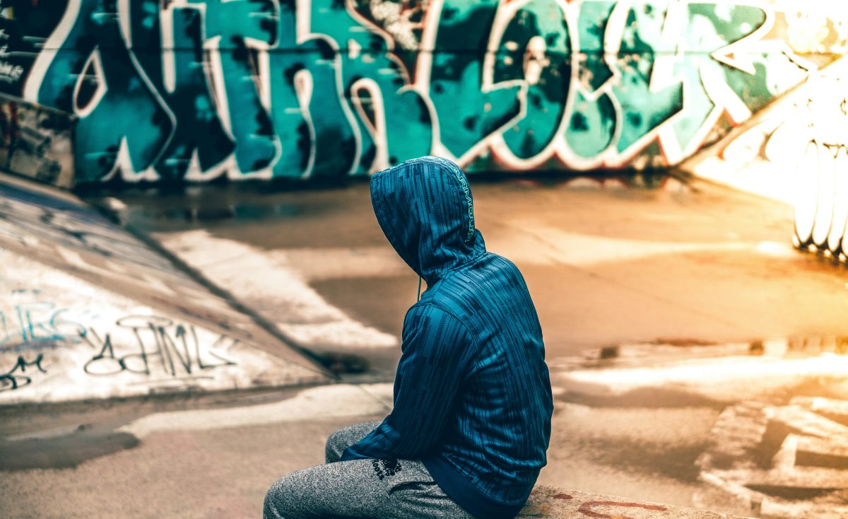 a person in a blue jacket sitting near a graffitied wall