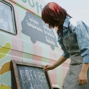woman writing coffee on chalk board outside of van