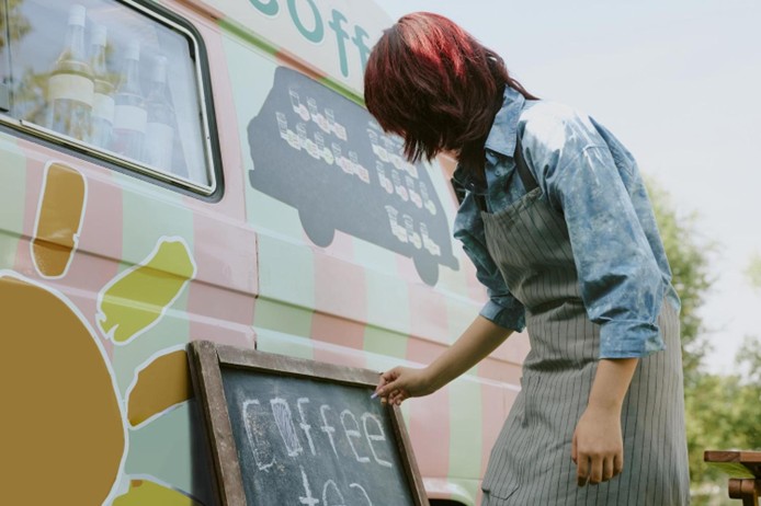 woman writing coffee on chalk board outside of van