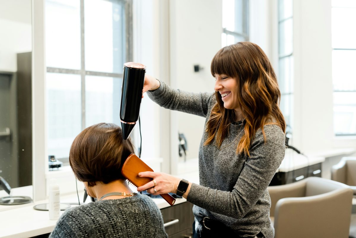 woman holding hair dryer and brushing a clients hair