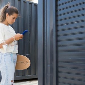 lady standing outside a storage unit holding a skateboard and a phone