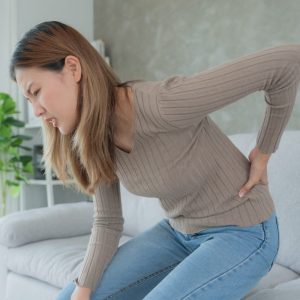 woman holding her lower back while sitting on a couch