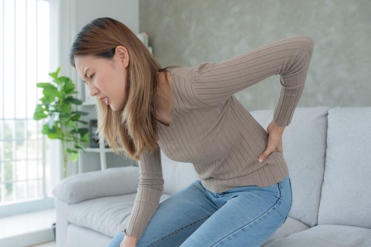 woman holding her lower back while sitting on a couch